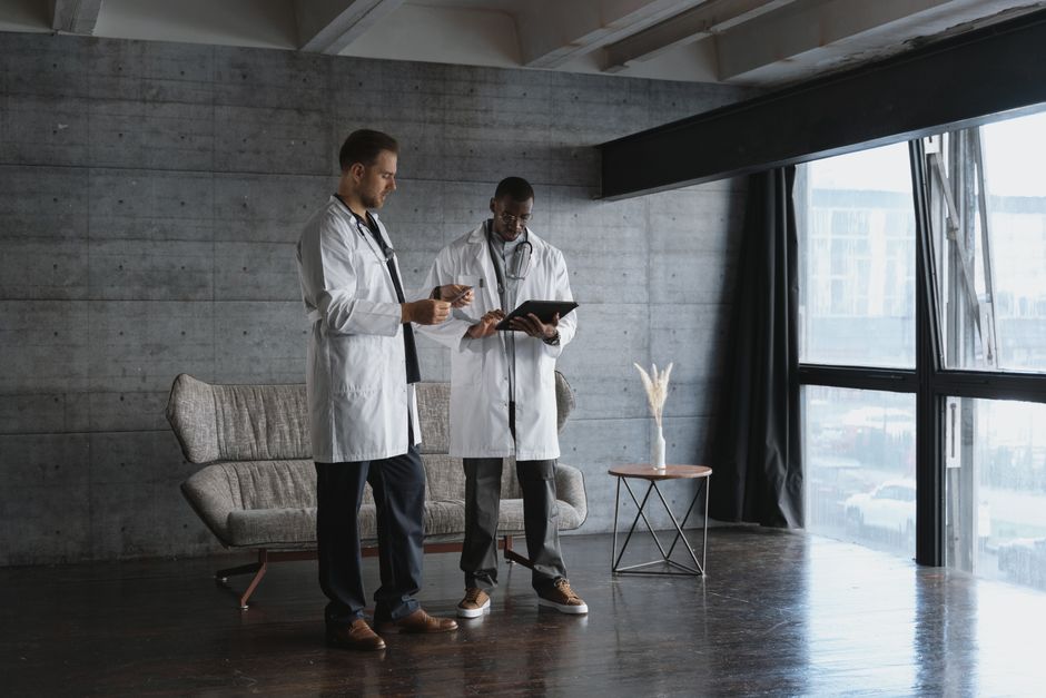 Two doctors in an industrial office discuss patient data on a digital tablet.